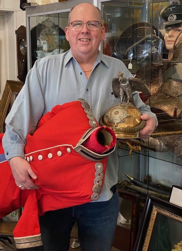 David Mattey standing in front of a showcase containing German Militaria .David is holding a guarde de corps helmet. 